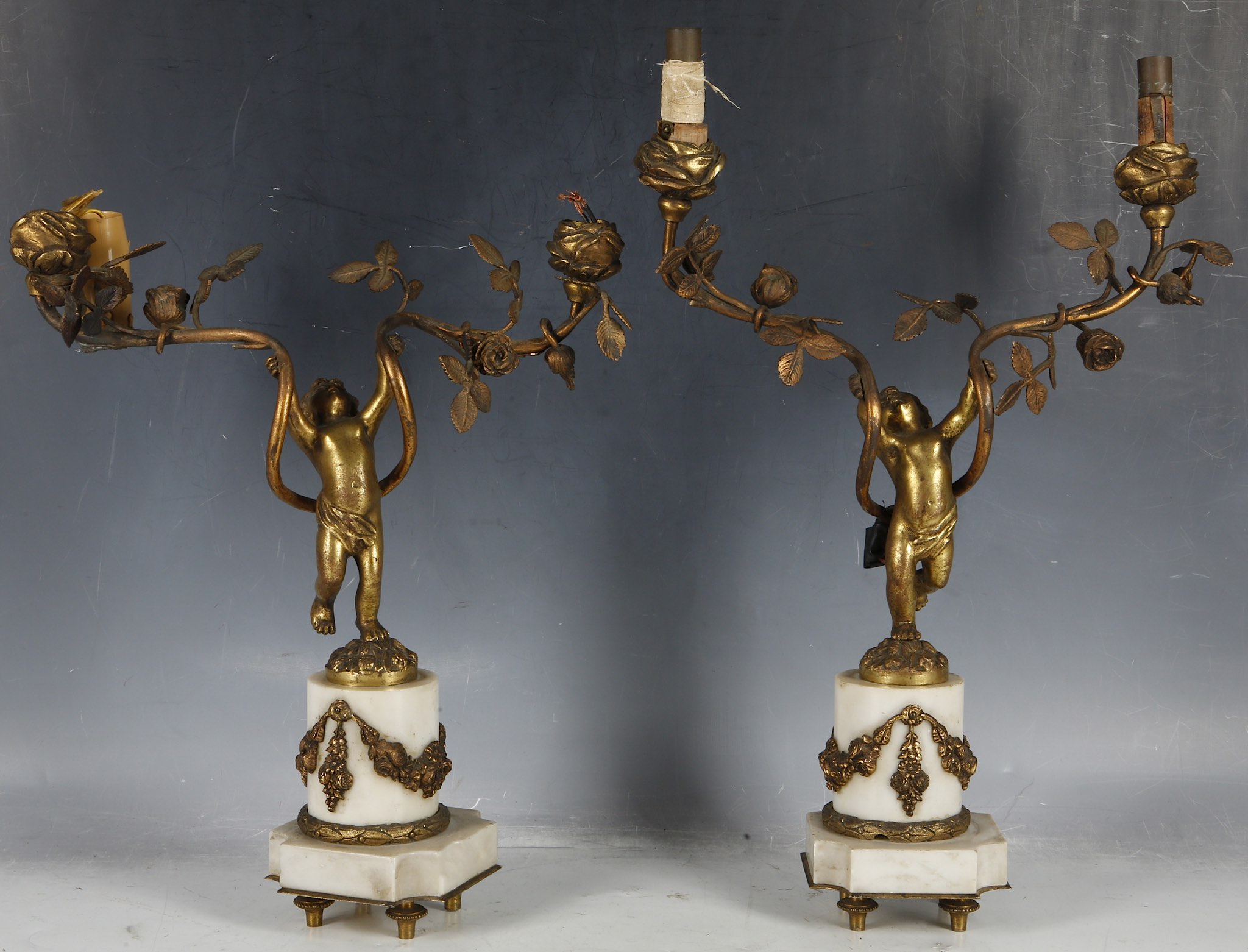 A pair of gilt metal two branch putti lights, putti mounted on white marble pedestal and plinth with
