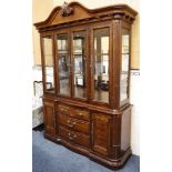 A contemporary walnut finish display cabinet with a scroll pediment and shell carving, four glass
