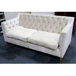 A beige upholstered button back two seater sofa, with contrasting scatter cushions, raised on square