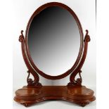 A Victorian mahogany vanity mirror, the oval plate on cheval supports over a serpentine base with