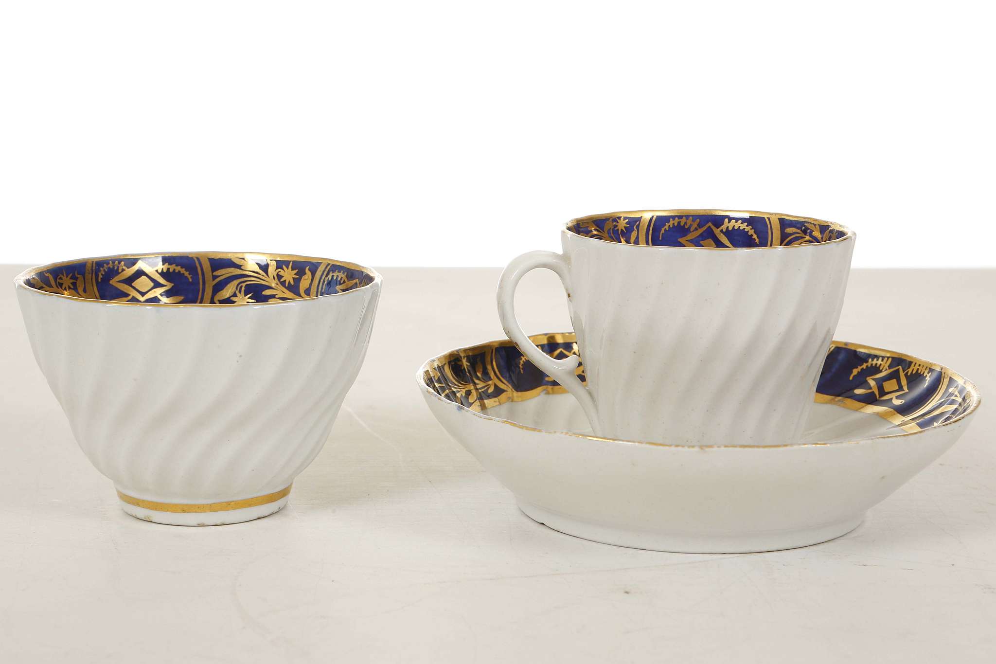 A COALPORT TRIO, circa 1800, each spiral-fluted and decorated with blue and gold borders, comprising