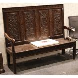 A mid 19th Century oak settle, arch border, four carved panels of stylised plants and fruit,