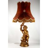 A gilt lamp in the form of a cherub holding a sconce, red shade edged in gold