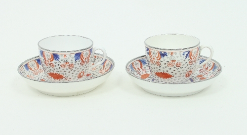 A pair of English porcelain teacups and saucers, circa 1800, painted blue and red, heightened in