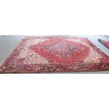 An Iranian wool carpet with central medallion on a red ground with white spandrels and guard stripe