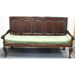 An 18th Century oak settle, the five fielded panel back and open arms on cabriole legs,