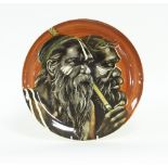 A Studio Pottery saucer shaped dish, painted Aborignes on a brown ground by Lavender Beard, 38cm