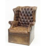 A brown leather button back wing armchair with panelled leather base