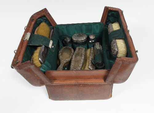 A leather dressing case containing silver topped and white metal topped brushes, glass bottles etc,