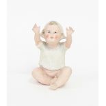 A bisque piano doll of a baby reaching upwards,