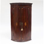 A George III mahogany bowfront corner cupboard, the twin doors each inlaid on oval,