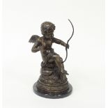 A bronze figure of Cupid, seated on a naturalistic base and set on a circular plinth,