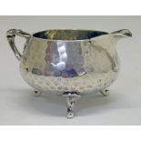 George V hammered silver cream jug in the Arts & Crafts style having a reeded handle and standing on