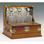 Early 20th Century brass mounted oak tantalus fitted three cut glass decanters, hinged compartment