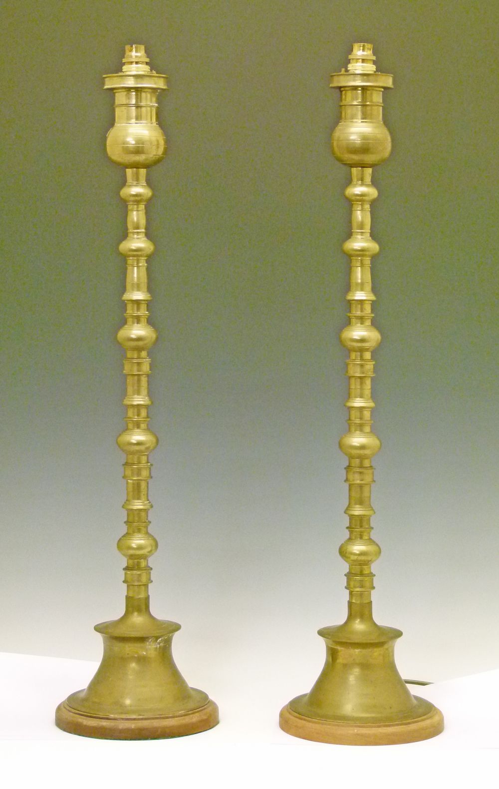 Pair of tall brass table lamps, each standing on a flared circular foot with an oak base, 80cm high