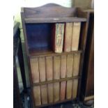 A small oak three tier bookcase containing a part set of Charles Dickens novels: The Imperial