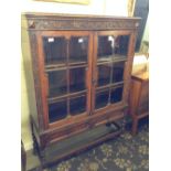 An early 20th century oak glazed bookcase with carved rosette decoration and two drawers under,