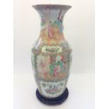 A Cantonese Famille Rose vase decorated with figures and foliage on carved wooden stand (17.5").