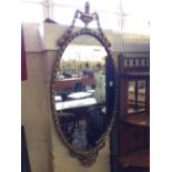 An oval gilt wood surround wall mirror with urn finial.