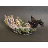 A German ceramic boat with griffin figure head and two cherubs to rear, encrusted with flowers,