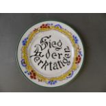 A Russian pottery plate with painted German inscription 'Sieg de Wektatien' and foliate surround,