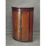 A George III oak and mahogany banded bow front hanging corner cupboard with ivory escutcheons and
