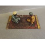 A cold painted bronze ornament in the form of two Moors seated on a rug playing a game, 4'' long
