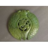 A Chinese circular green hardstone pendant carved in the form of an insect with a dragon to