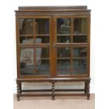 Early 20th century oak bookcase enclosed by two glazed doors on barley twist stand, W106cm,