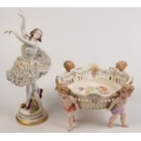 A German porcelain ballerina figure and a German porcelain bowl supported by four cherubs, damages.