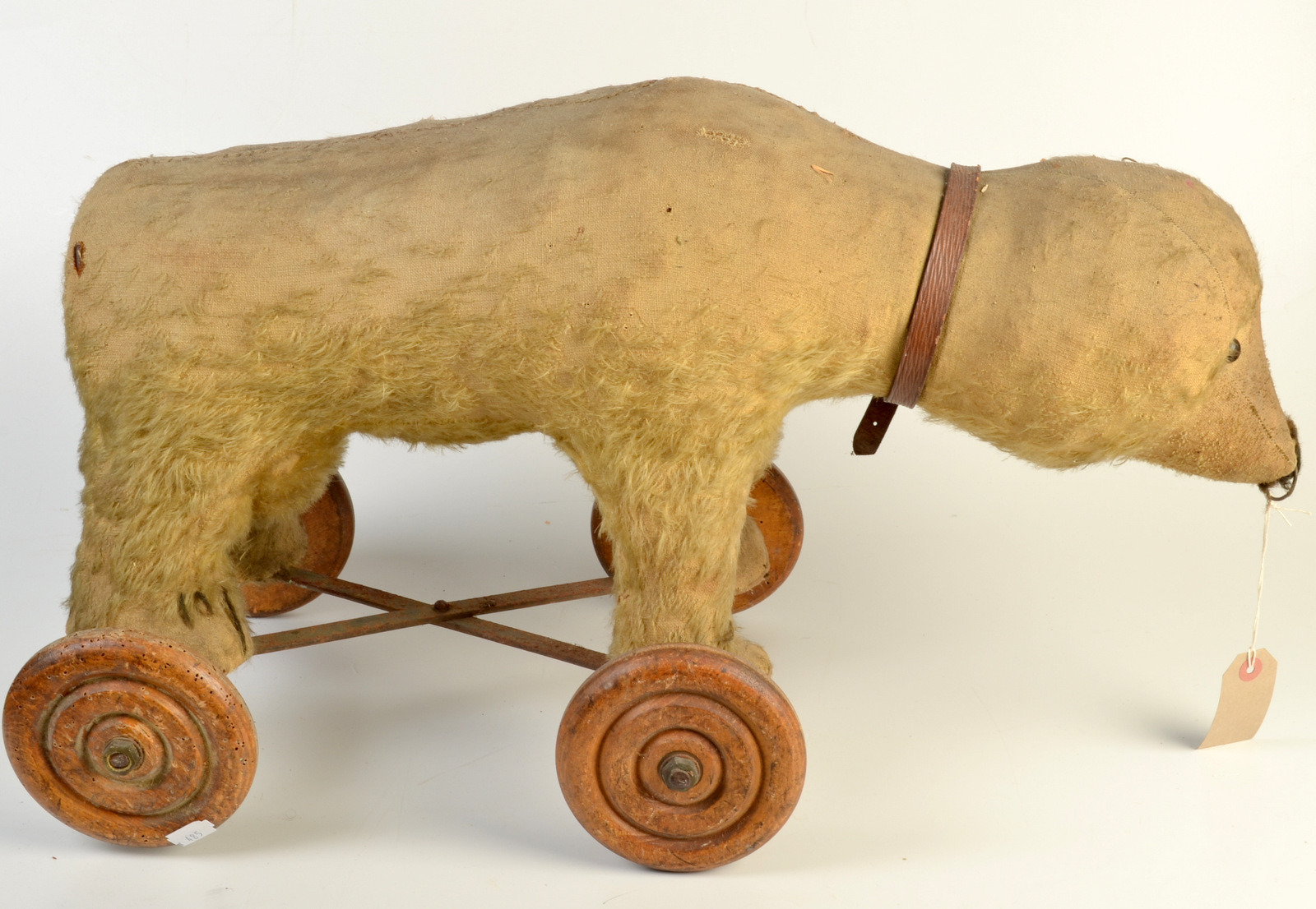 An early 20th century pull along toy bear on iron carriage with four turned wheels,