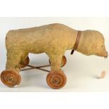 An early 20th century pull along toy bear on iron carriage with four turned wheels,