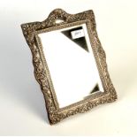 A rectangular table mirror, the Edwardian silver frame embossed with scrolls and flowers,