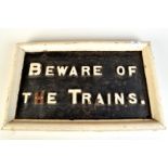 A railway sign "Beware of the Trains" the iron letters painted white on black painted wooden