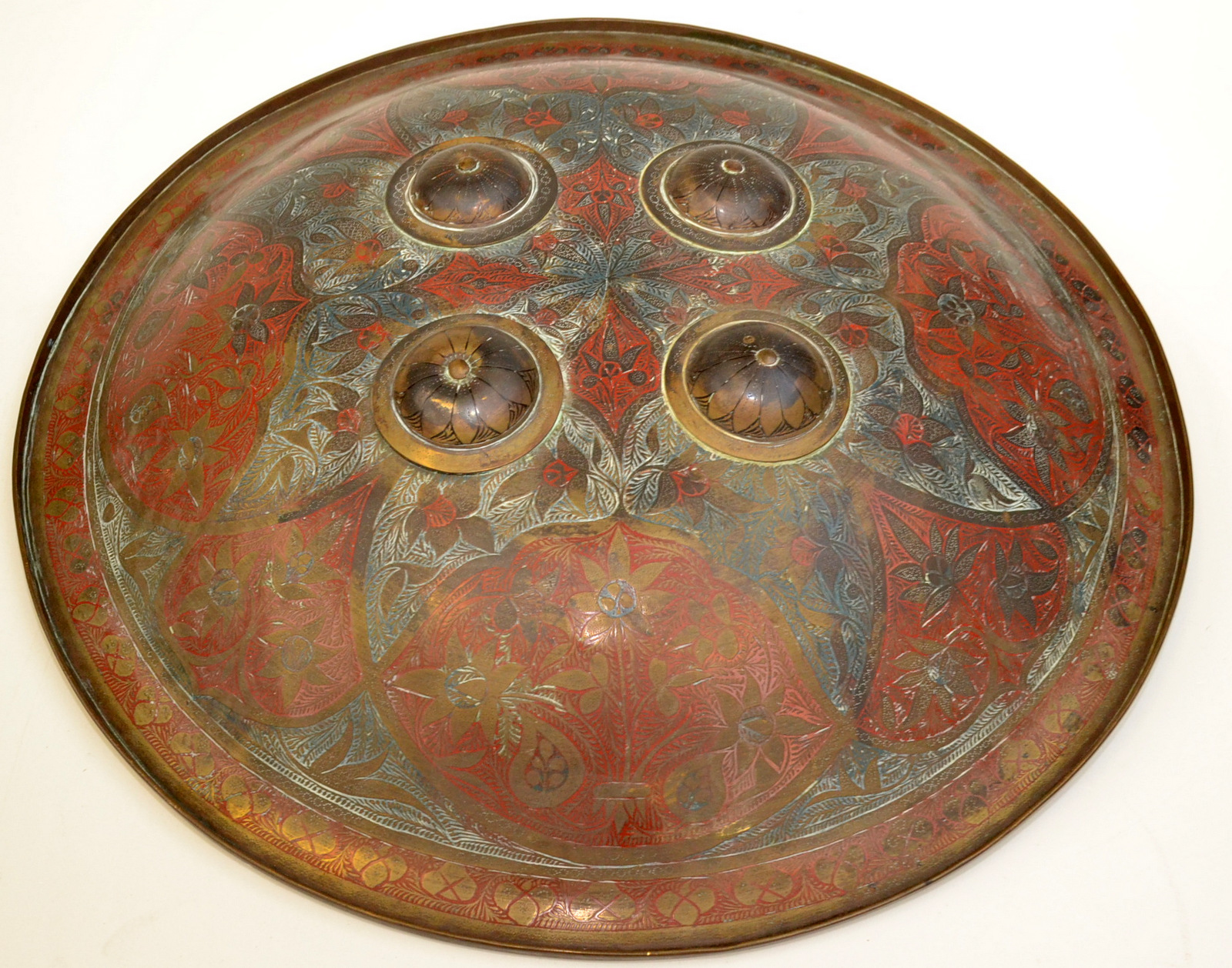 An Indian brass Dahl shield patterned with a foliate design and with four raised bosses.