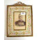 A gilt brass and embroidered photograph frame with a portrait of a senior military gentleman.