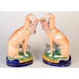 A pair of Staffordshire models of seated greyhounds, each with a hare in its mouth. 24.5cm.