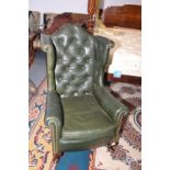 A buttoned green leather wing armchair with squat cabriole legs.