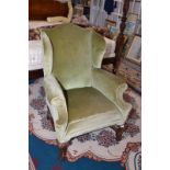 A wing armchair in Queen Anne style with moulded cabriole legs and low shaped stretchers.