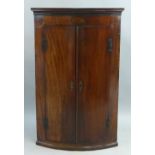 An early 19th Century mahogany quadrant corner cupboard, wall hanging with flared cornice over an