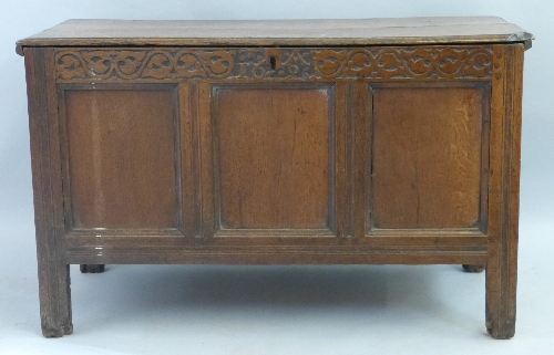 An 18th Century oak chest, the hinged lid over three panelled fascia having scroll carved frieze,