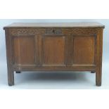 An 18th Century oak chest, the hinged lid over three panelled fascia having scroll carved frieze,