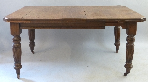 A late 19th Century oak extending dining table, the wind out canted oblong top with one leaf on