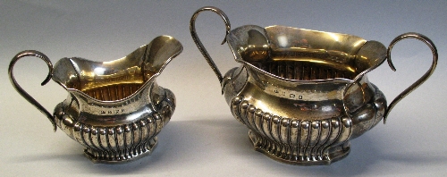 An Edwardian sugar bowl, of bulbous quatrefoil form with half reeded body and two scrolling loop