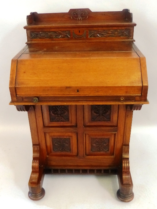 A late 19th/early 20th Century walnut davenport, the raised back with carved front and hinged top