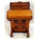A late 19th/early 20th Century walnut davenport, the raised back with carved front and hinged top