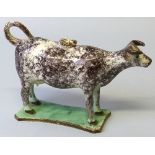 A 19th century sponged creamware cow creamer, with tail loop handle and lid, on green glazed