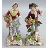 A pair of Sitzendorf figures, the boy and girl wearing bright clothes and holding baskets of flowers