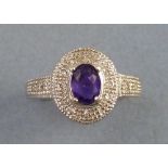 An amethyst and diamond ring, having oval amethyst in raised setting on a textured oval bed inset