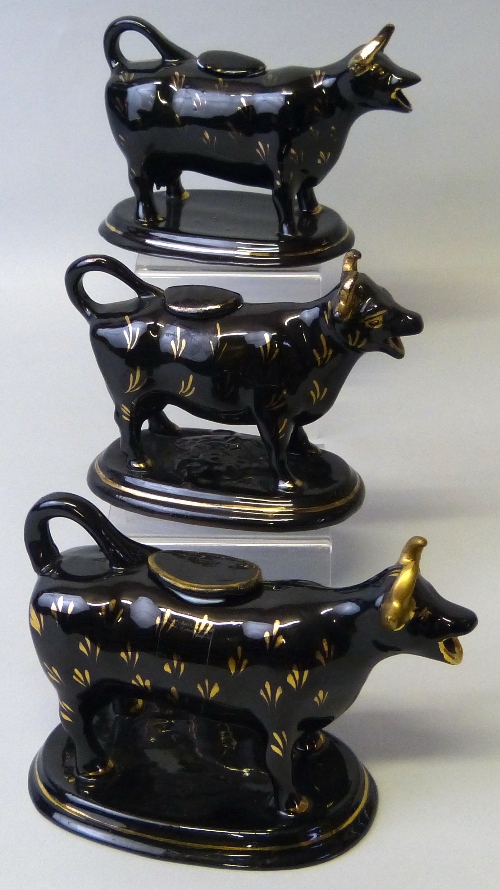Three 19th century Staffordshire black glazed cow creamers, each with tail loop handle and lid and